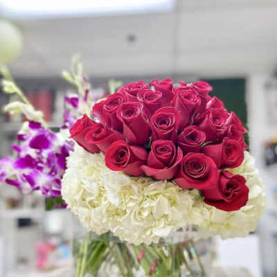 Red roses arranged over white hydrangeas with purple orchids in a clear square glass vase