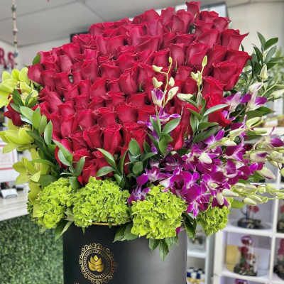Large hatbox arrangement of red roses with green hydrangeas and purple orchids in a black round box