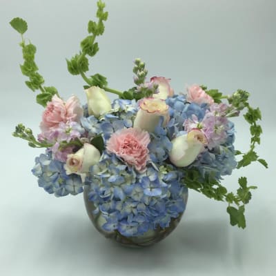 Blue hydrangea arrangement with pink carnations and white roses in a glass vase