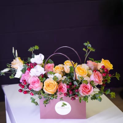 Pink and yellow roses arranged in a mauve gift bag