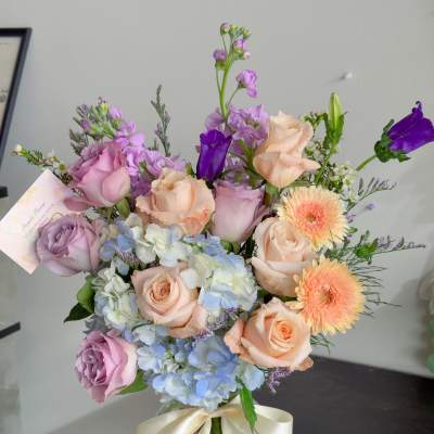 Bouquet of pastel roses, hydrangeas, and purple blooms in a glass vase