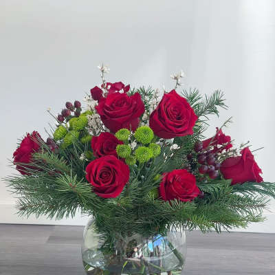 Red roses in a glass vase with pine and small white accents