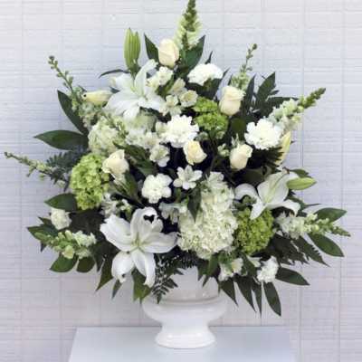 White lilies and roses arranged in a white pedestal vase
