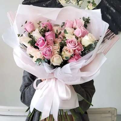 Bouquet of pink and white roses wrapped in pale paper with a ribbon