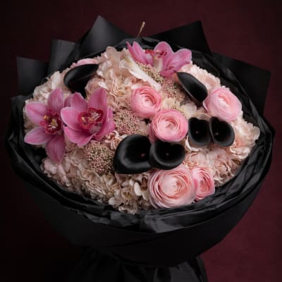 Pink bouquet with orchids, ranunculus, and pale hydrangeas wrapped in black paper