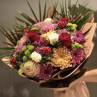 Bouquet of red roses, chrysanthemums, and white blooms wrapped in paper