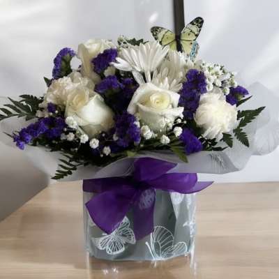 White roses and purple flowers in a wrapped bouquet with a purple ribbon