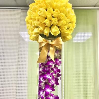 Tall glass vase with submerged purple orchids and a dome of yellow roses tied with a satin bow.