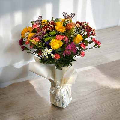 Mixed bouquet of yellow, pink, and burgundy flowers wrapped in cream paper