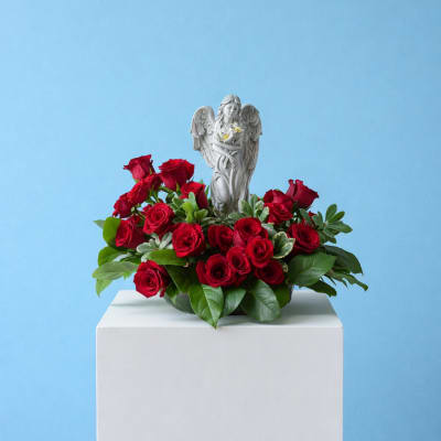 Red roses arranged around a small angel figurine on a white pedestal
