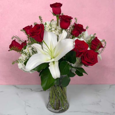 Red roses and a white lily in a clear glass vase.