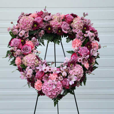 Heart-shaped floral wreath on a black stand with pink and purple blooms
