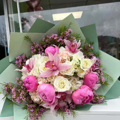 Bouquet of pink peonies, orchids, and white roses wrapped in green paper