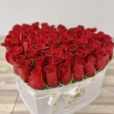 Heart-shaped white box filled tightly with red roses and tied with a cream ribbon