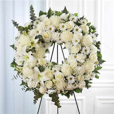 White floral wreath on a black stand with lilies, roses, and daisies