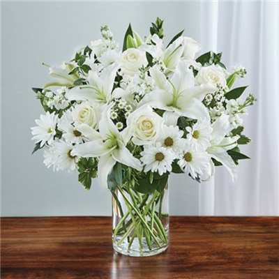 White lilies, roses, and daisies in a clear glass vase