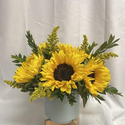 Sunflower arrangement in a pale blue vase on a wooden stand
