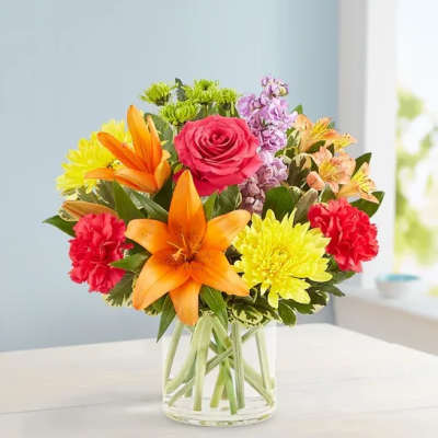 Mixed bouquet with orange lilies, pink rose, and yellow chrysanthemums in a glass vase