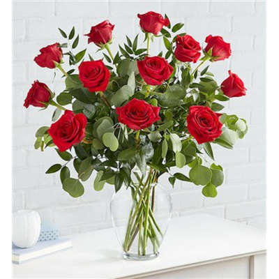 Red roses arranged in a clear glass vase with greenery