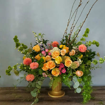 Large mixed flower arrangement in a gold vase with peach and pink blooms