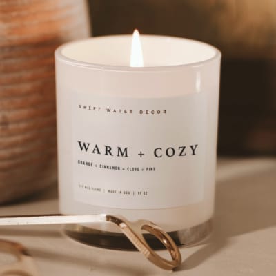 Lit white candle in a glass jar with a metal wick trimmer