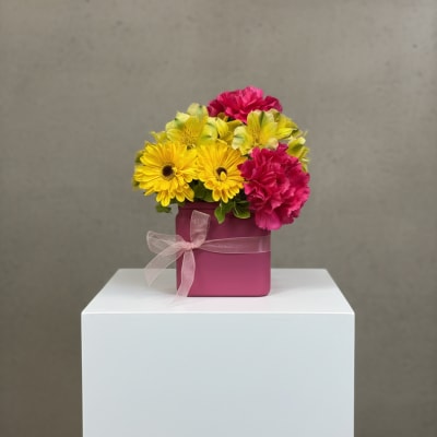 Pink and yellow flowers arranged in a magenta box with a ribbon