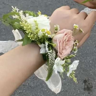 Two wrists wearing small floral corsages with pink and white flowers