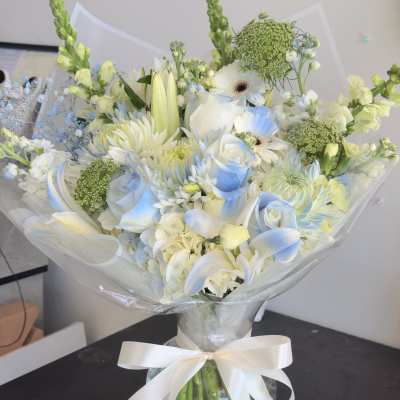 White and pale blue bouquet in a glass vase with a ribbon bow