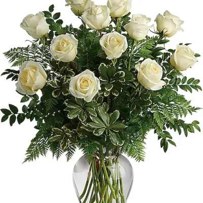 White roses arranged in a clear glass vase with dense greenery