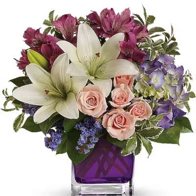 Bouquet of white lilies, pink roses, and purple flowers in a purple glass vase
