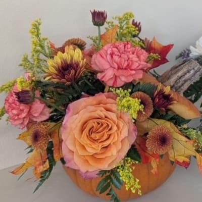 Autumn floral arrangement with peach roses and pink blooms in a pumpkin container