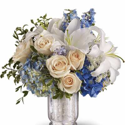 White lilies and cream roses in a glass vase with blue hydrangeas