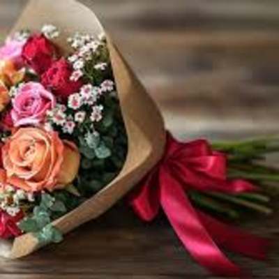 Bouquet of pink, peach, and red roses wrapped in brown paper with a red ribbon