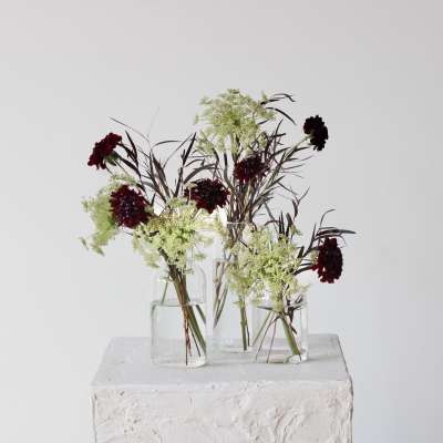 Three small glass vases hold dark red flowers with airy white filler.