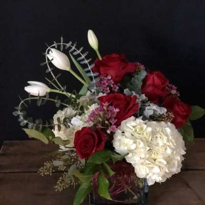 Red roses and white hydrangea in a glass vase with white tulips