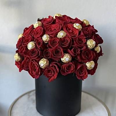 Red roses arranged with gold-wrapped chocolates in a black box