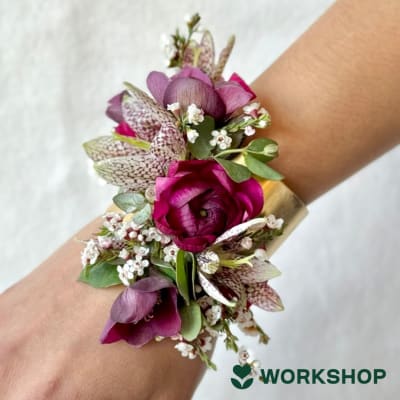 Purple floral wrist corsage with small white blossoms and a gold cuff