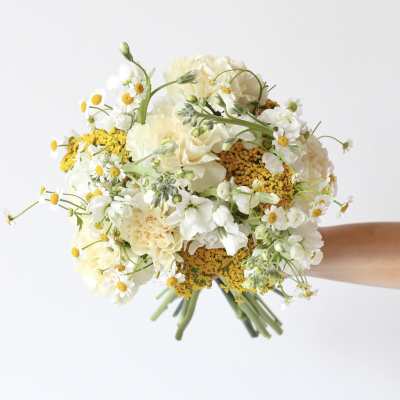 Handheld bouquet of white and pale yellow flowers with small daisy blooms