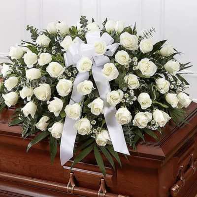 White rose casket spray with a white ribbon on a wooden casket