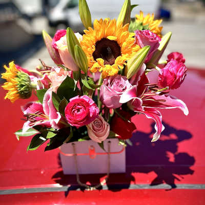 Bright bouquet of pink roses, lilies, and sunflowers in a white box