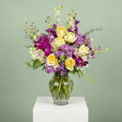 Yellow roses and purple orchids in a clear glass vase