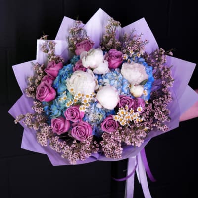 Bouquet of pink roses, blue hydrangeas, and white peonies wrapped in lavender paper