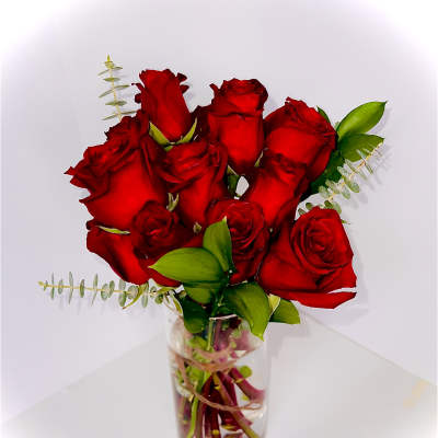 Red roses arranged in a clear glass vase with small greenery accents