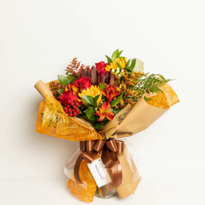 Bouquet of red and yellow flowers wrapped in tan paper with a brown ribbon