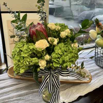 Bouquet of green hydrangeas, cream roses, and a pink protea in a glass vase