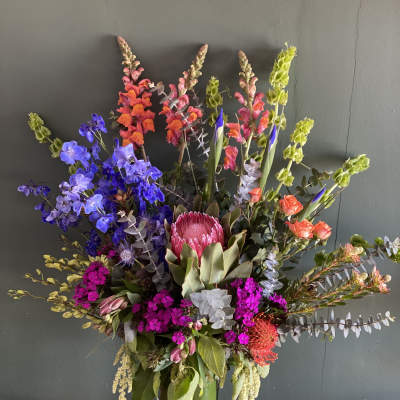 Tall mixed flower arrangement in a green vase with bright pink, blue, and orange blooms