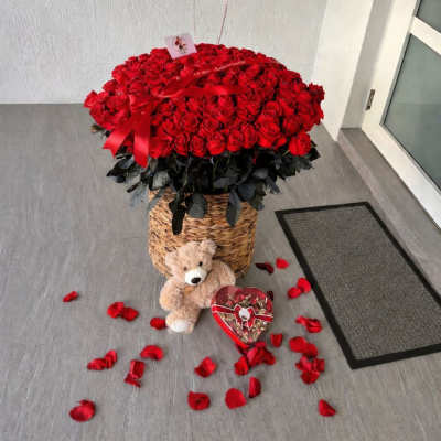 Basket of red roses with heart balloons, teddy bear, and candy box