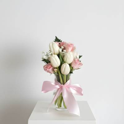 Pink roses and white tulips in a glass vase with a pink ribbon