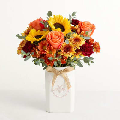 Bouquet of sunflowers, roses, and mums in a white vase with a ribbon