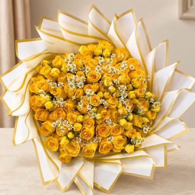 Bouquet of yellow roses with small white daisies wrapped in white paper with gold trim